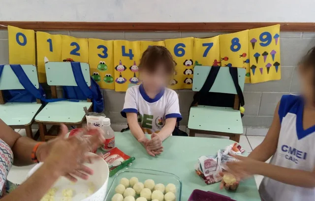 Menina na aula de culinária da escola, fazendo bolinhas de massa com a turma